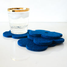 White background with four light blue flower coasters laid out and a gold-rimmed glass filled with ice and a fizzy drink sitting on one of the coasters for scale. The coasters are made of 1/4" thick wool design felt and have a slight textured appearance.