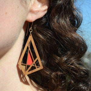 Medium toned cherry wood geometric earrings on curly brown haired model. Shown with gold french hooks with sections painted in metallic gold, bright red and aqua.