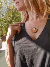 Model in black shirt wearing a brown wood and metallic gold semicircle necklace by Bird of Virtue