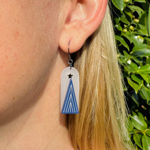 Model wearing a white arched earring with blue and silver christmas tree and cut out star  by Bird of Virtue