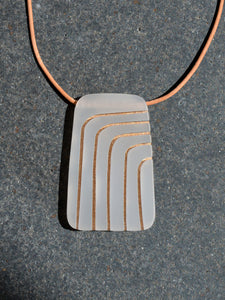 Rectangular gray pendant with curved gold lines on leather cord necklace, photographed on grey stone surface