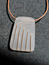 Rectangular gray pendant with curved arch gold lines on leather cord necklace, photographed on black stone surface