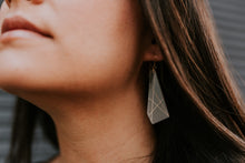 A close-up lifestyle shot of a woman wearing a geometric, faceted clear acrylic dangle earring with thin gold wire crisscross patterns.