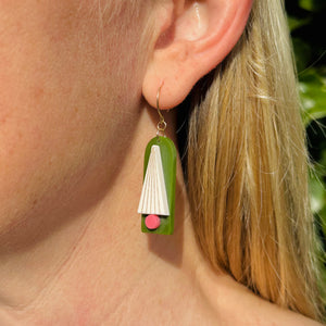 Model wearing a green arched earring with a white tree with metallic gold lines and pink trunk by Bird of Virtue