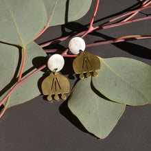 Pair of brass and silver earrings on a branch with green leaves