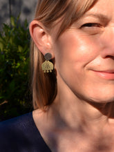 Close-up of a woman wearing brass floral earrings with a blurred natural background