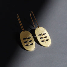 Pair of brass leaf-shaped earrings on a dark background