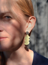 Close-up of a woman wearing brass earrings with a blurred background