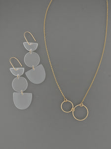 Gold necklace with two small gold circles shown with frosted white triple geo shaped earrings on a grey background by Bird of Virtue