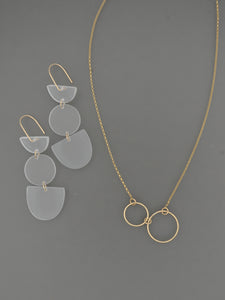 Gold necklace with two small gold circles shown with frosted white triple geo shaped earrings on a grey background by Bird of Virtue