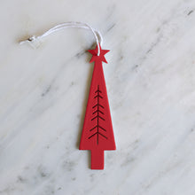 A minimalist red Christmas tree ornament with a white hanging string, displayed on a white marble surface.