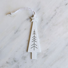 A minimalist white Christmas tree ornament with a hanging loop, resting on a white marble surface.