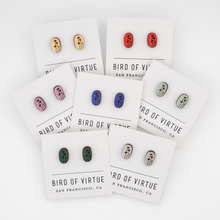 Seven pairs of oval wooden earrings from Bird of Virtue, each with black floral stem designs on different colored backgrounds.