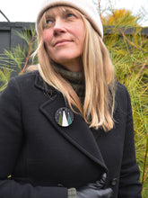 Person wearing a black coat with a tree-themed round brooch, standing outdoors.