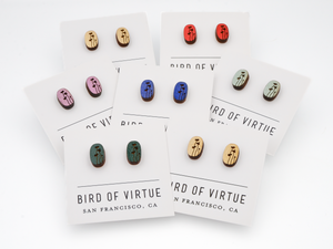 Seven pairs of oval wooden earrings from Bird of Virtue, each with black floral stem designs on different colored backgrounds.