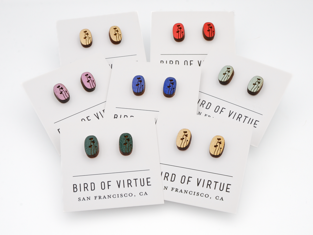 Seven pairs of oval wooden earrings from Bird of Virtue, each with black floral stem designs on different colored backgrounds.