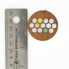 Wooden pendant with hexagonal design next to a metal ruler for scale