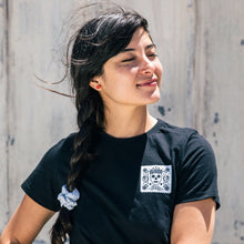 Dark haired model wearing black t-shirt with her eyes closed, facing into the sun. Wearing red rectangle Bird of Virtue stud earrings  Edit alt text