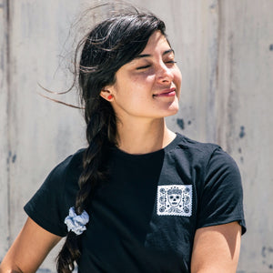 Dark haired model wearing black t-shirt with her eyes closed, facing into the sun. Wearing red rectangle Bird of Virtue stud earrings  Edit alt text