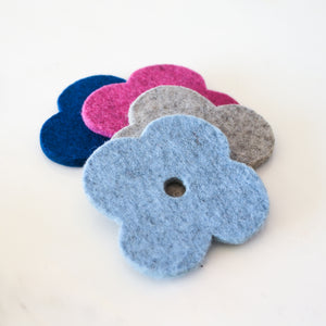 White background with four colorful flower coasters laid out in colors light blue, pink, navy and grey. The coasters are made of 1/4" thick wool felt and have a slight textured appearance.