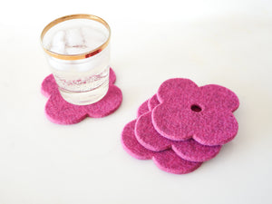 White background with four pink flower coasters laid out and a gold-rimmed glass filled with ice and a fizzy drink sitting on one of the coasters for scale. The coasters are made of 1/4" thick wool design felt and have a slight textured appearance.