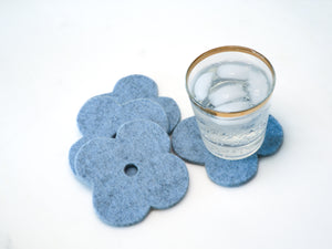 White background with four light blue flower coasters laid out and a gold-rimmed glass filled with ice and a fizzy drink sitting on one of the coasters for scale. The coasters are made of 1/4" thick wool design felt and have a slight textured appearance.