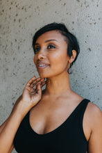 Dark skinned woman wearing black tank top and bronze circle earring 