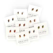 Assortment of colorful, offset rectangle-shaped wooden stud earrings on white Bird of Virtue cards against a white background. Colors are silver, moss, gold, leaf, poppy, midnight, dogwood, rouge, sky blue
