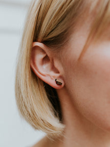 Detail shot of small offset rectangle stud earring on light-skinned short-haired blond model's ear. 