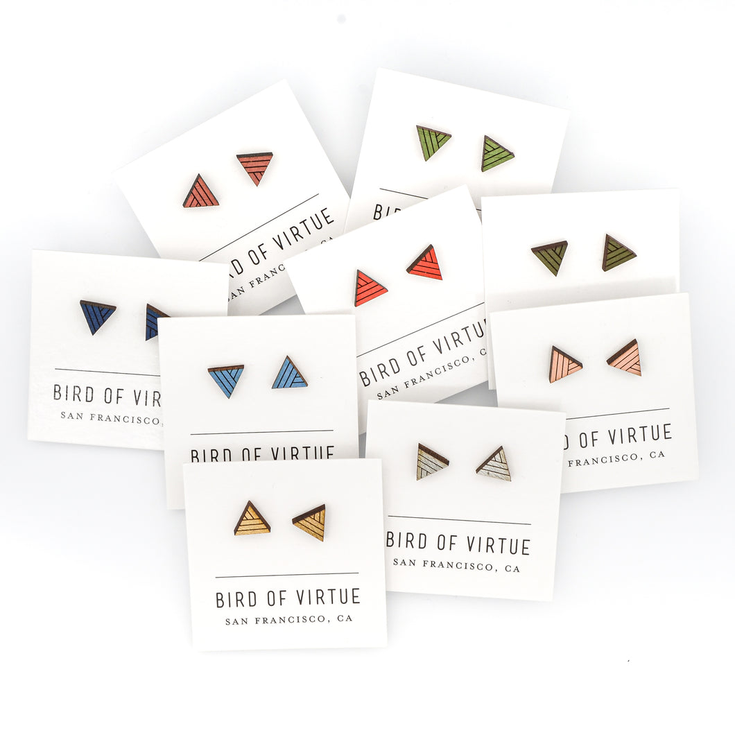Assortment of colorful triangle-shaped wooden stud earrings on white Bird of Virtue card against a white background. Colors are silver, moss, gold, leaf, poppy, midnight, dogwood, rouge, sky blue