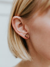 Detail earlobe shot of of triangle-shaped, small geometric patterned stud earring on light-skinned, short-haired blond model. 