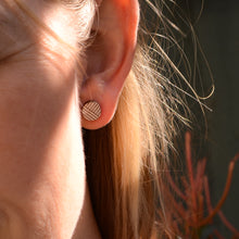 Detail shot of of small geometric patterned round stud earring on light-skinned blond model's ear. 