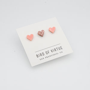 white background with pink and rose glitter heart shaped stud earrings on white card