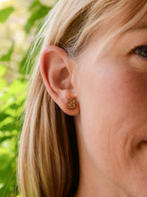 Closeup of small gold rectangle earring on along model's ear with green leaves in background. Made by Bird of Virtue