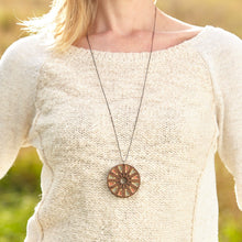 Woman in Cream sweater with long circle walnut wood necklace and greenery behind.